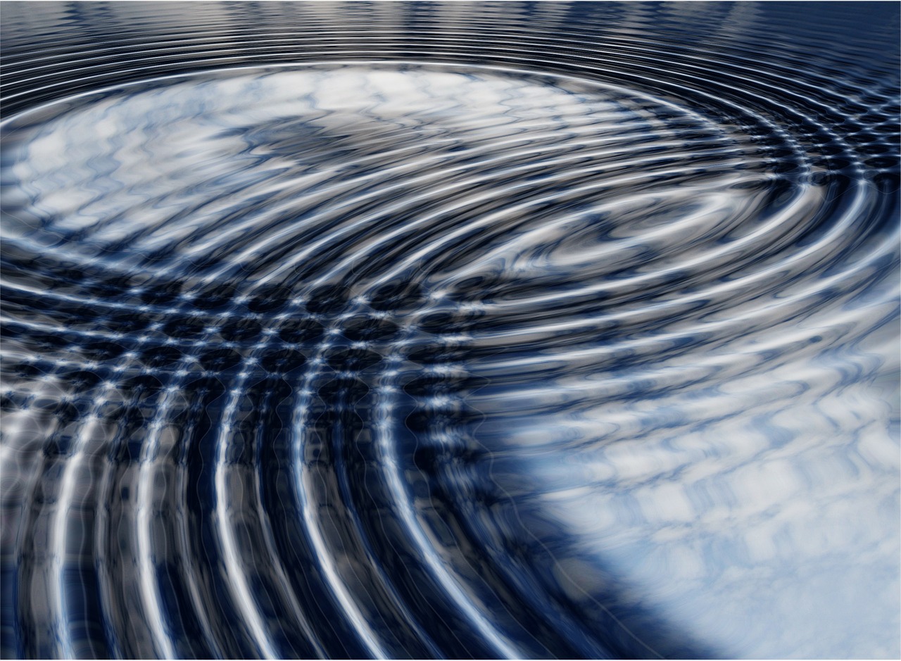 Two sets of circular ripples spreading across dark water and crossing one another, so that where they meet the crests and troughs interlock into a regular lattice of bright and dark patches.